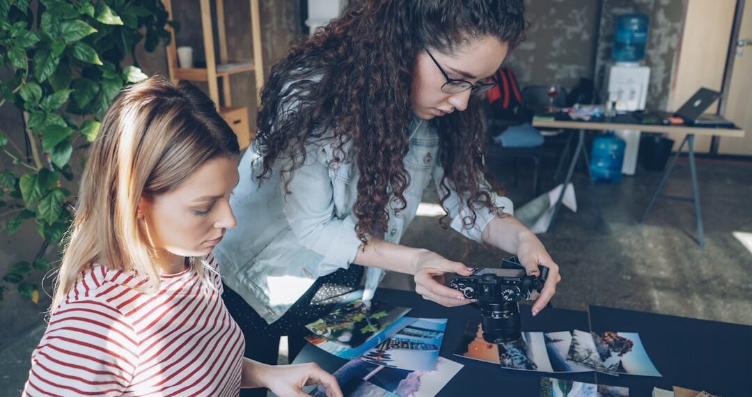 Creative colleagues placing pictures on table and shooting flat lay while talking about designing project. Top view of modern table with illustrations, notebooks and markers.