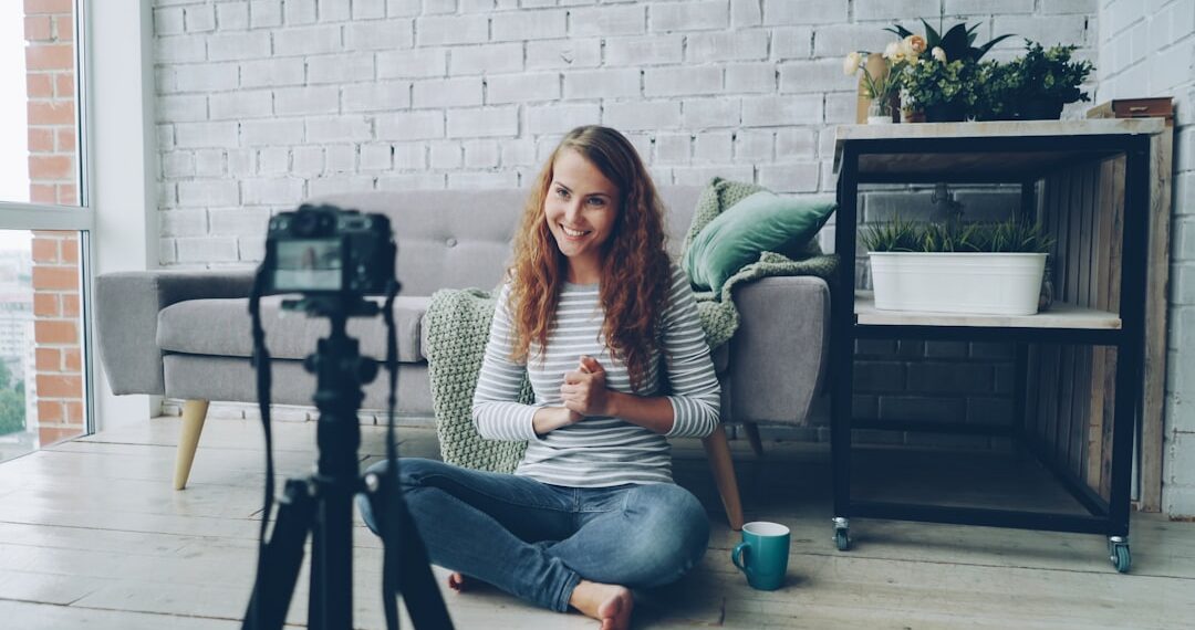 Happy female blogger is recording video for internet videolog talking and gesturing showing thumbs-up and waving hand. Blogging, young people and success concept.