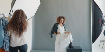 African-American woman model working with stylist and photographer indoors in studio wearing trendy clothing and headwear. People and photography concept.