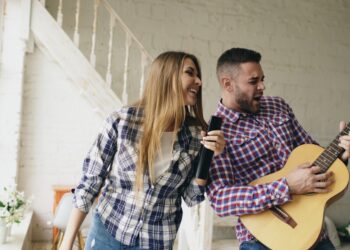 Funny happy and loving couple dance on bed singing with tv controller and playing guitar. Man and woman have fun during holiday at home